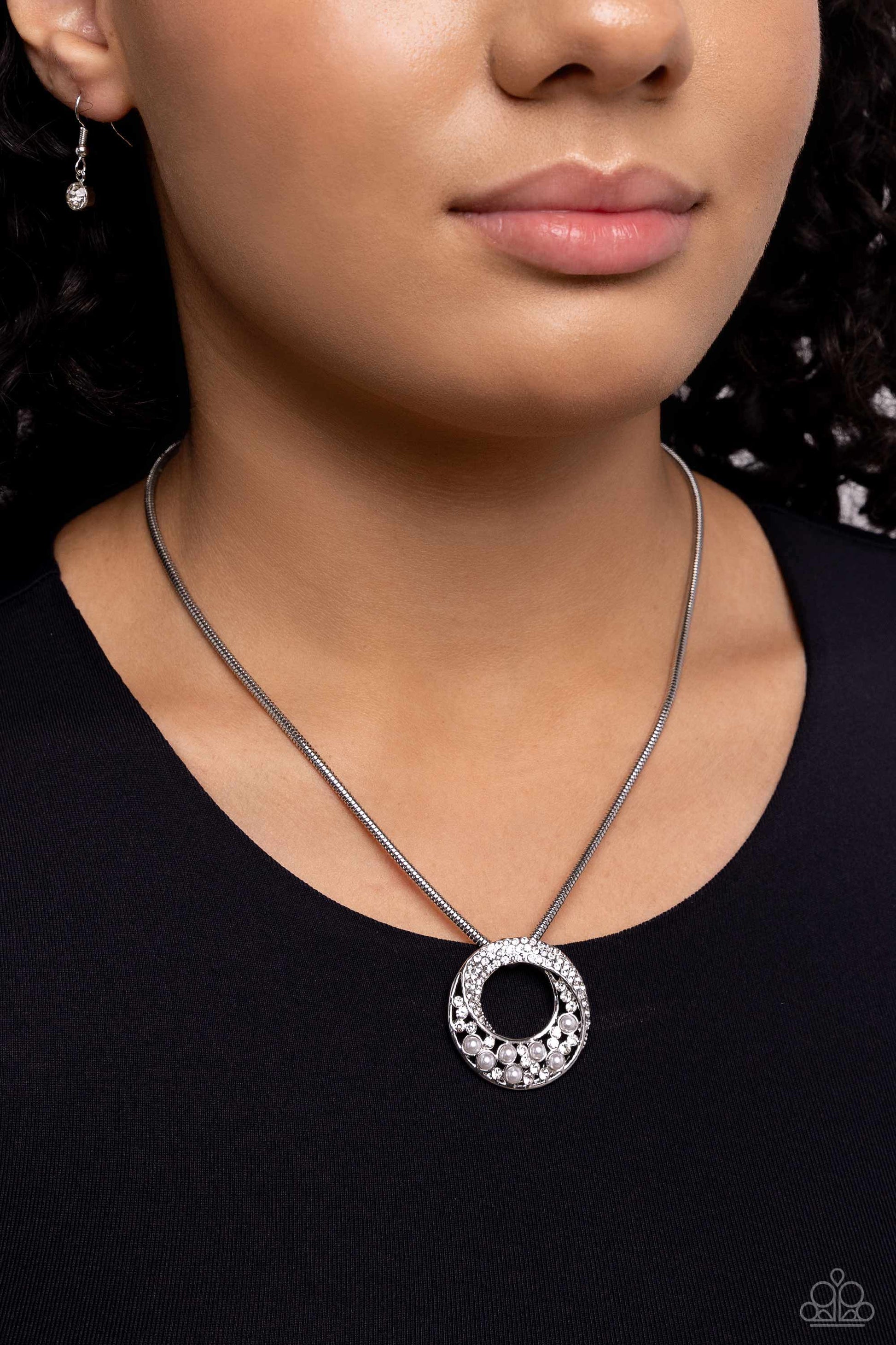 Necklace with a circular pendant worn by a person against a dark background
