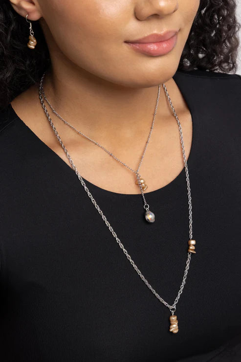 Close-up of a woman wearing a layered necklace with small pendants on a black background