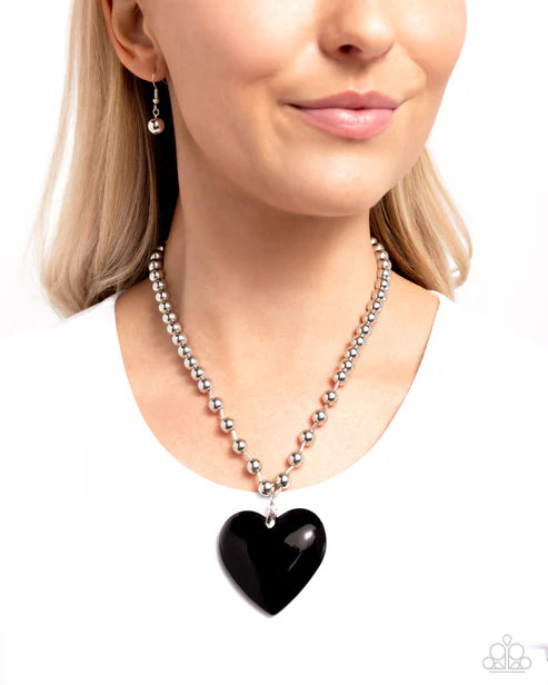 Necklace with a black heart pendant worn by a model on a white background
