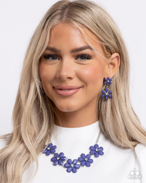 Woman wearing a white top with a blue floral necklace and earrings on a white background