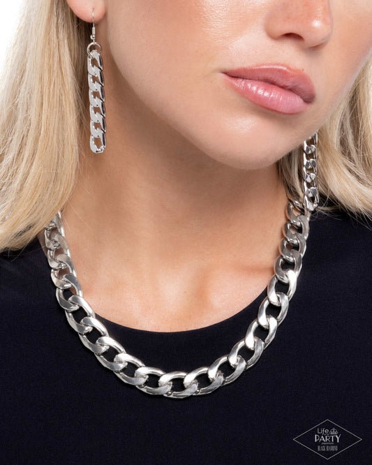 Close-up of a person wearing a silver chain necklace and earrings.