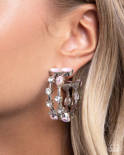 A close-up of a model's ear wearing a silver-toned triple-hoop earring adorned with light pink faceted gemstones and clear rhinestones.