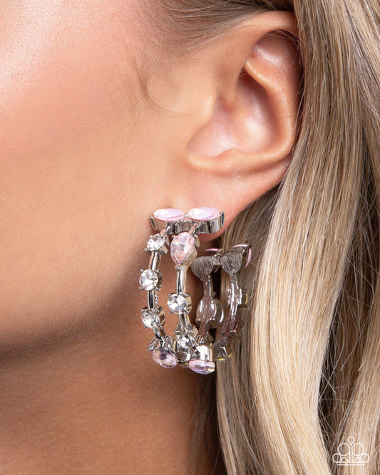 A close-up of a model's ear wearing a silver-toned triple-hoop earring adorned with light pink faceted gemstones and clear rhinestones.