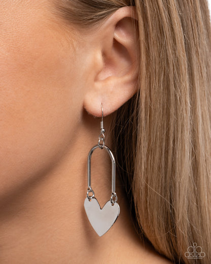 Silver heart-shaped earring worn by a person with light brown hair.