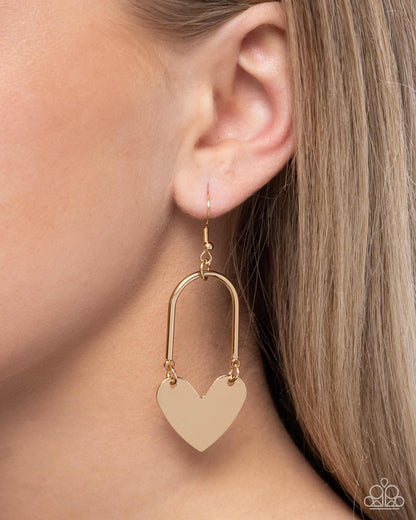 Gold heart-shaped earring worn by a person with light brown hair.