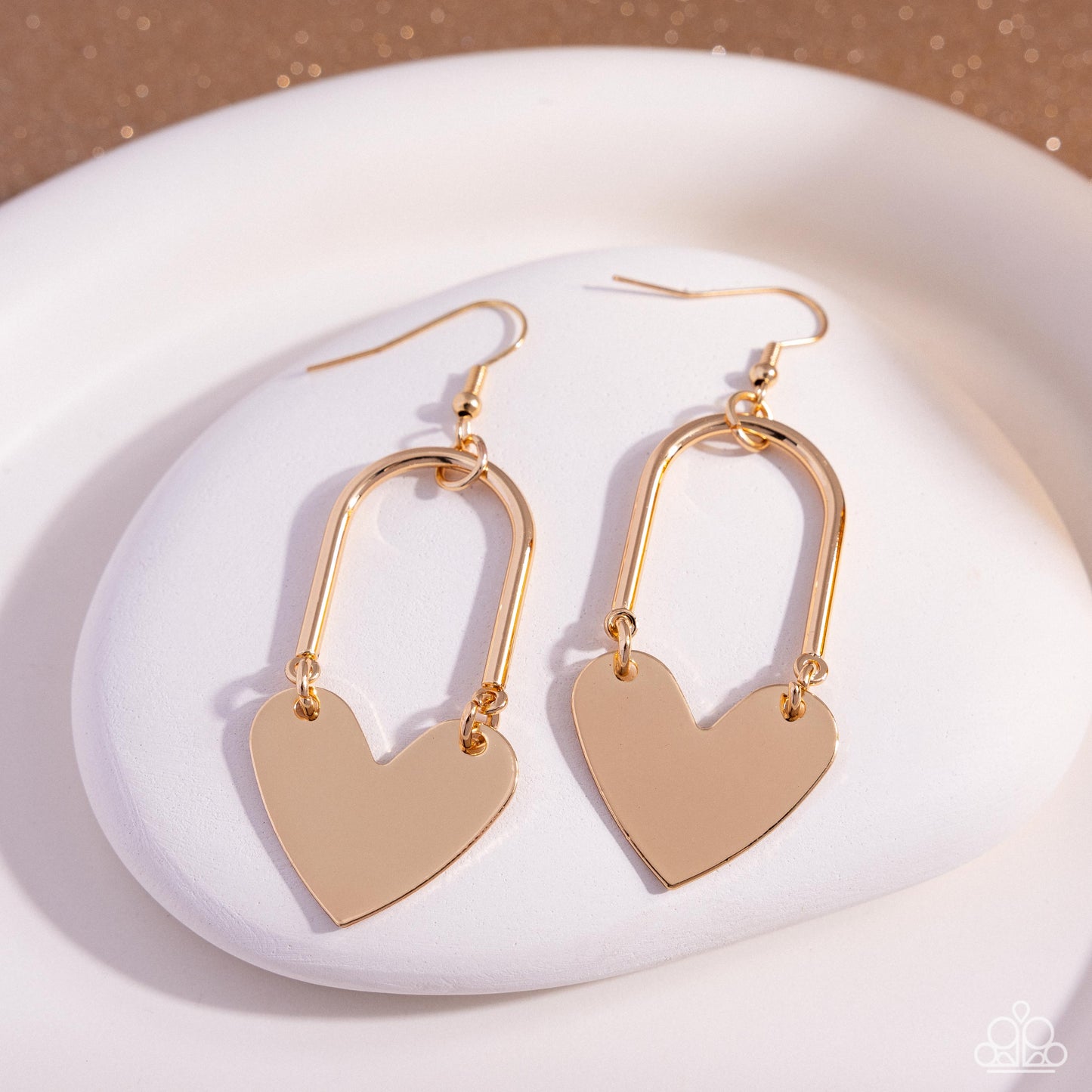 Gold heart-shaped earrings on a white plate with a beige background