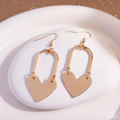 Gold heart-shaped earrings on a white plate with a beige background