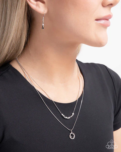 Close-up of a person wearing a silver necklace and earrings on a plain background