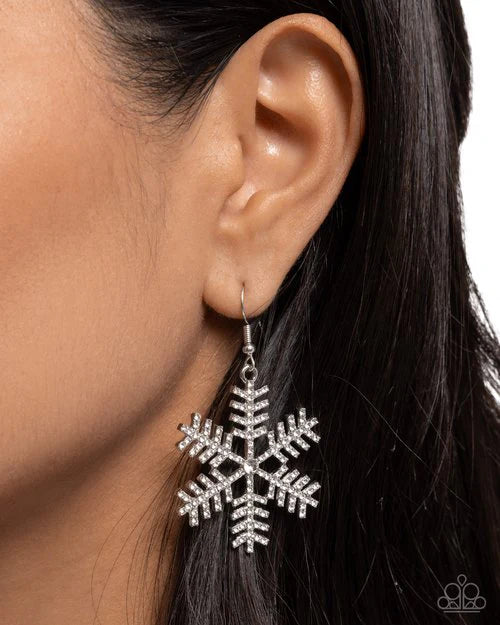 Silver snowflake earring worn by a person with dark hair on a white background