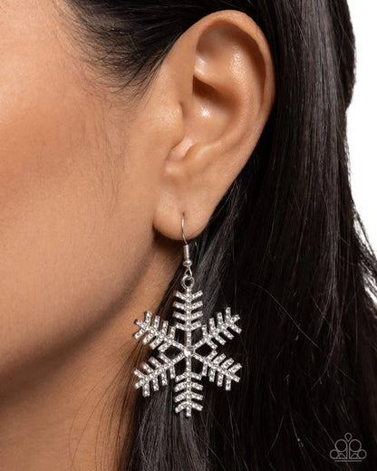 Silver snowflake earring worn by a person with dark hair on a white background