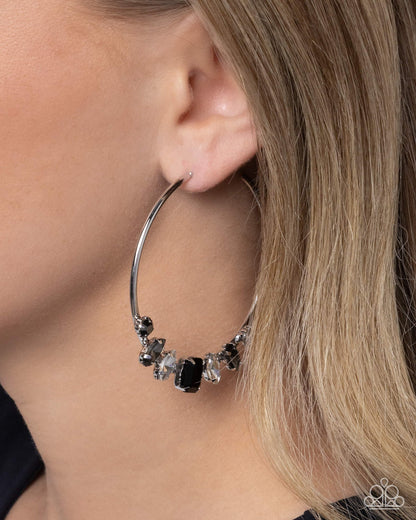 Close-up of a silver hoop earring with embedded stones worn by a person.