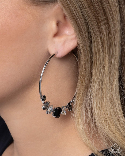 Close-up of a silver hoop earring with embedded stones worn by a person.