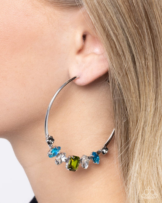 Close-up of a hoop earring with colorful gemstones worn by a person.
