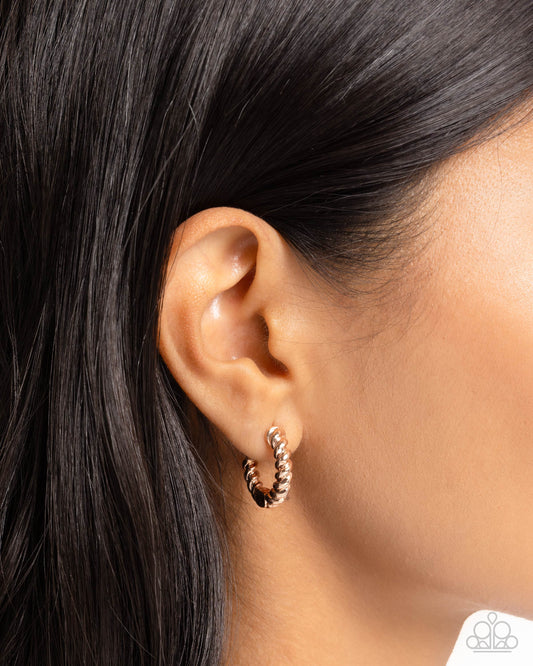 Close-up of an ear wearing a gold hoop earring with a blurred background