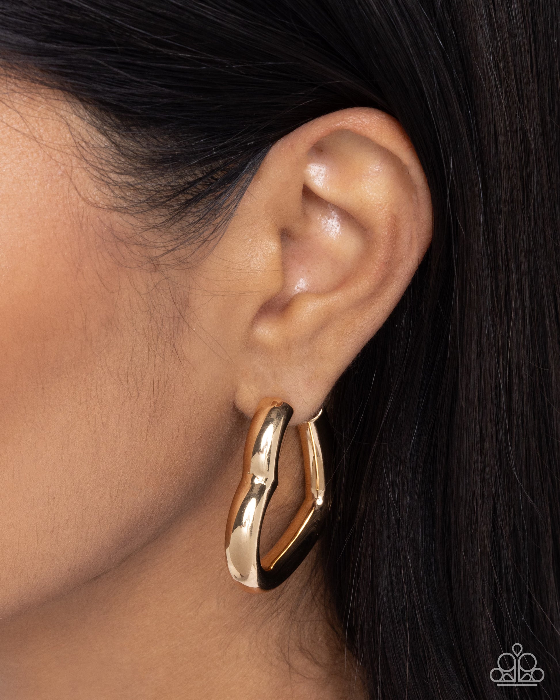 Gold hoop earring worn by a person with dark hair