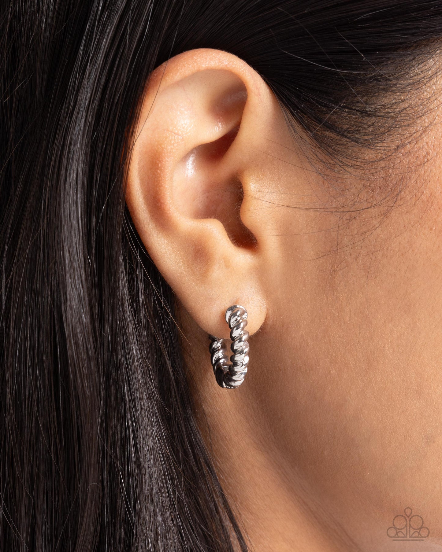 Close-up of an ear wearing a silver hoop earring with a blurred background