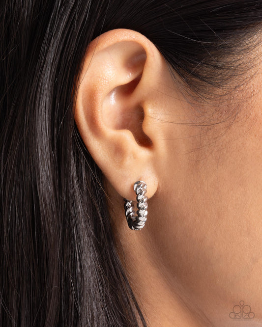 Close-up of an ear wearing a silver hoop earring with a blurred background