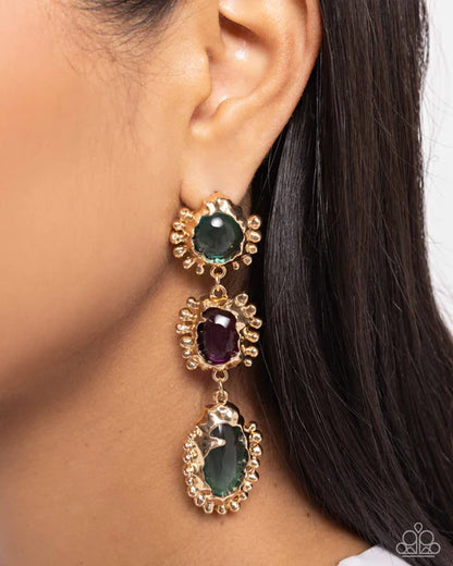 Gold earrings with green and purple gemstones worn by a person with dark hair.