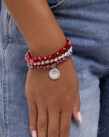 Red beaded bracelet with a silver charm on a wrist against a denim background