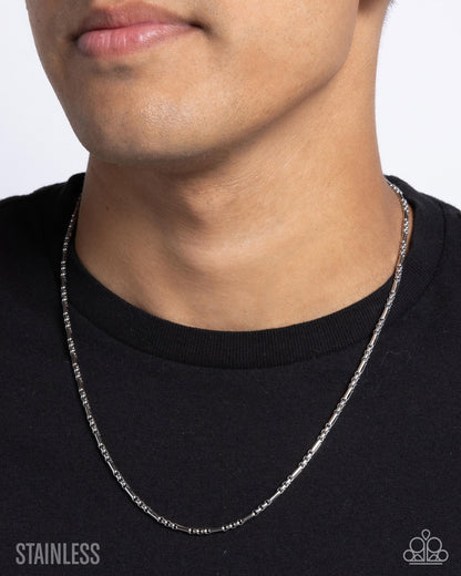 Person wearing a silver chain necklace against a plain background