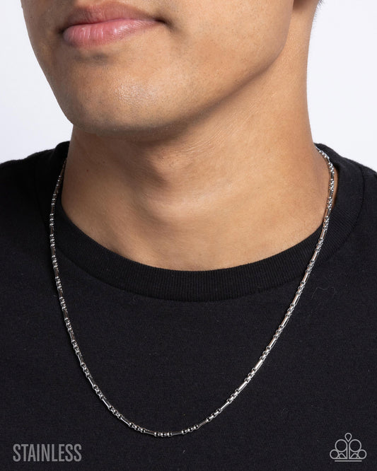 Person wearing a silver chain necklace against a plain background