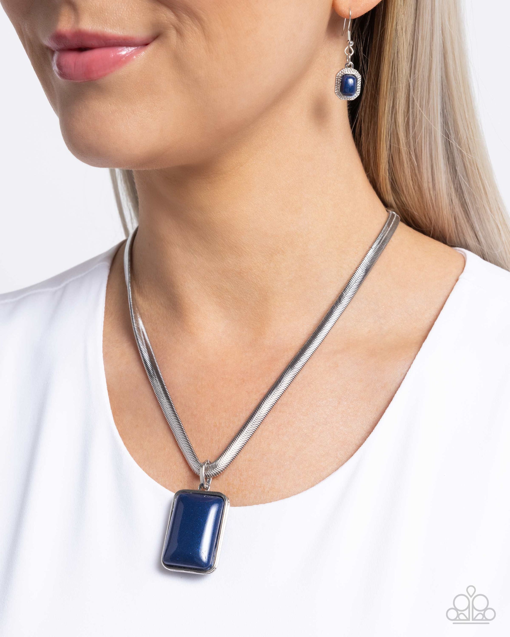 Woman wearing a silver necklace with a blue pendant and matching earrings on a white background