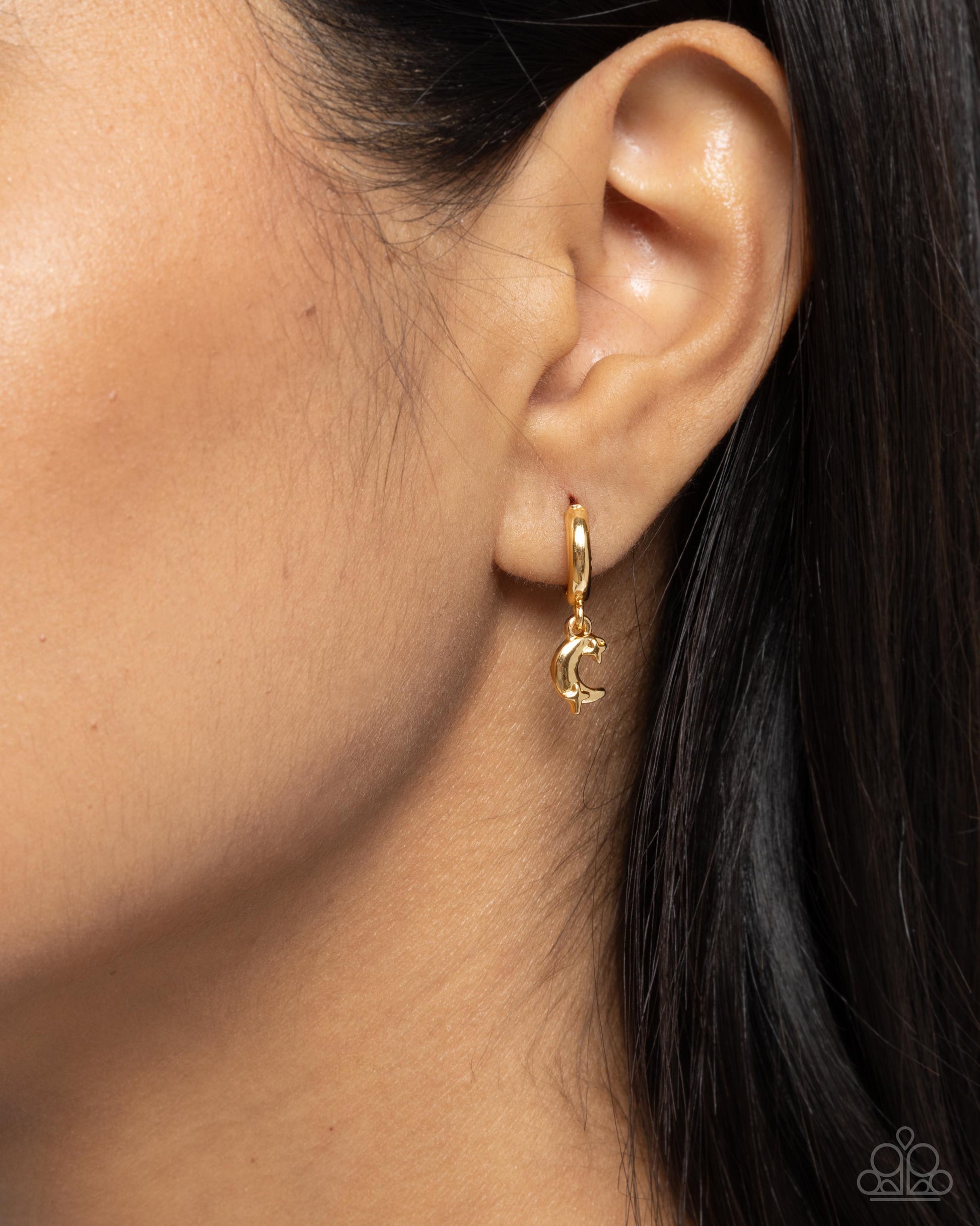 Gold hoop earring with a small crescent moon charm worn by a person.