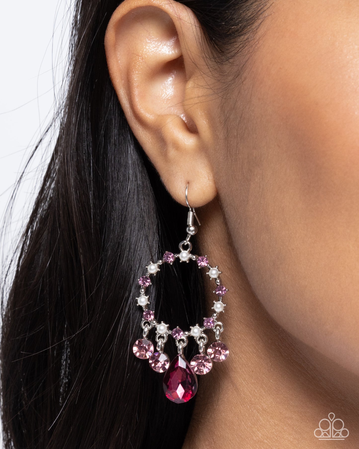 Close-up of an ear wearing a pink and silver hoop earring with a red gemstone.