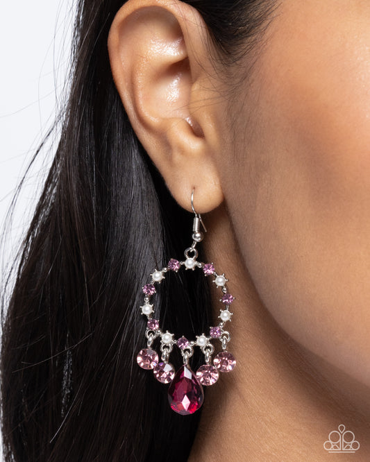 Close-up of an ear wearing a pink and silver hoop earring with a red gemstone.
