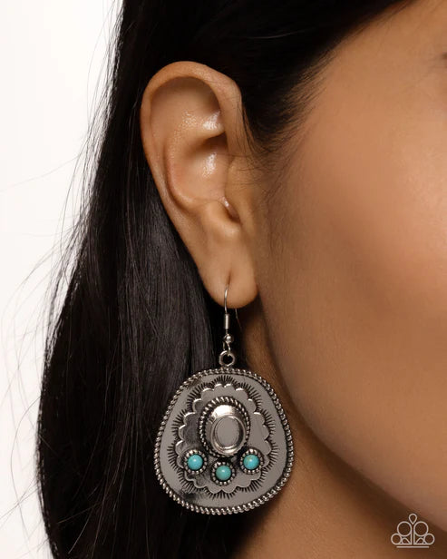Close-up of an ear wearing a silver earring with turquoise stones on a white background