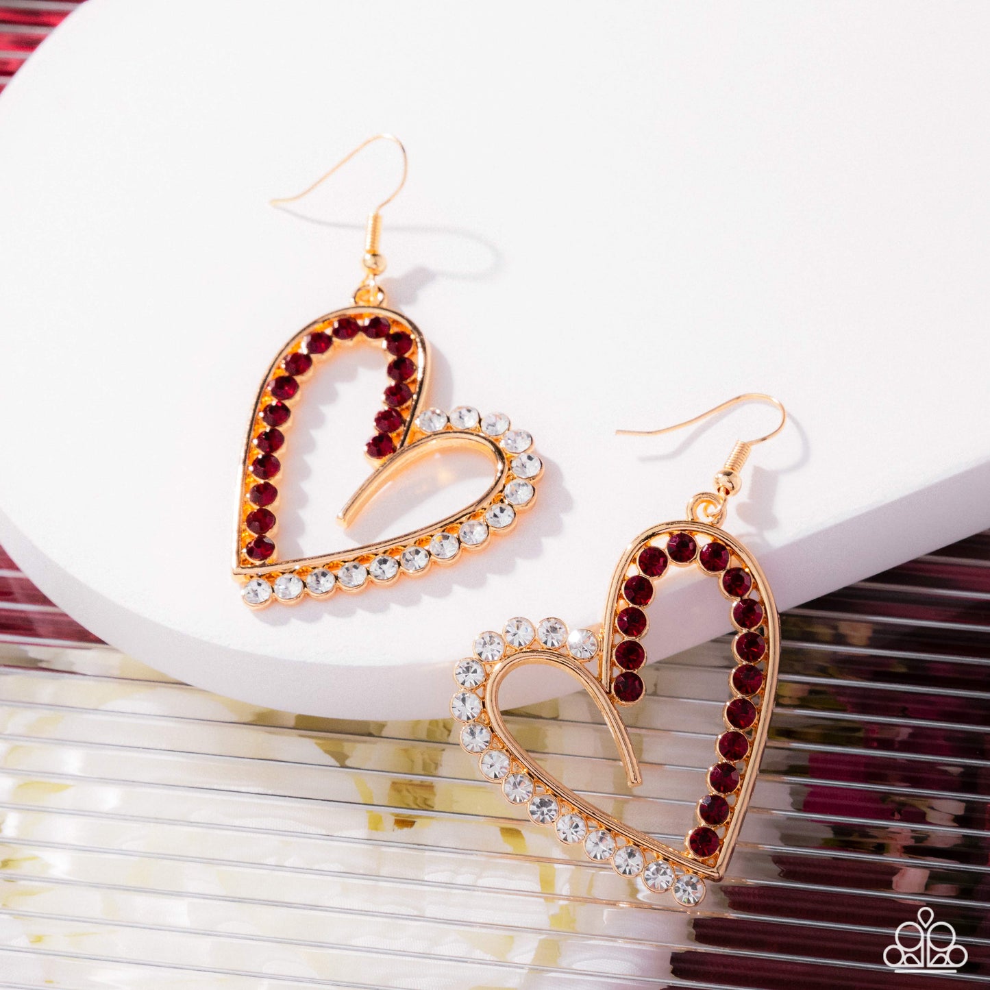 Heart-shaped earrings with red and clear gemstones on a white surface