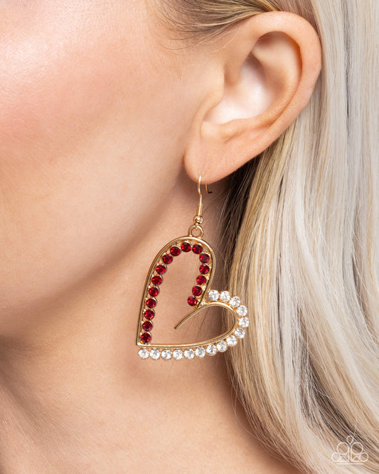 Heart-shaped earring with red and clear stones worn by a person with blonde hair.