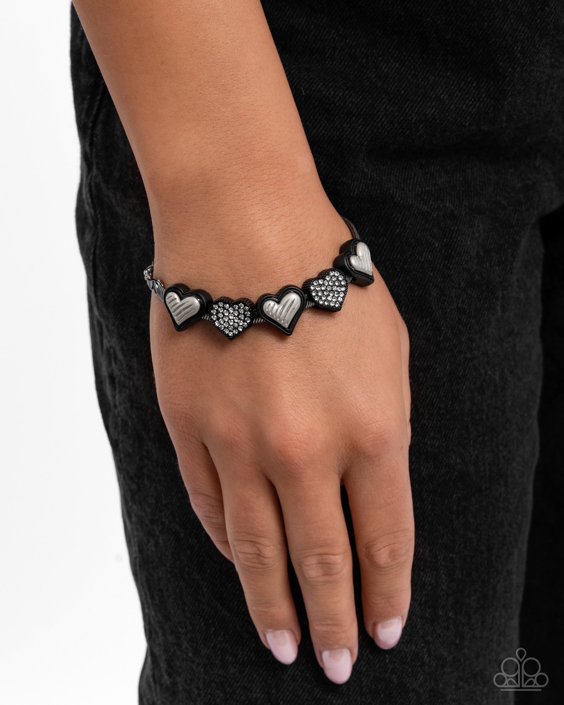 Bracelet with heart-shaped charms on a wrist against a black background