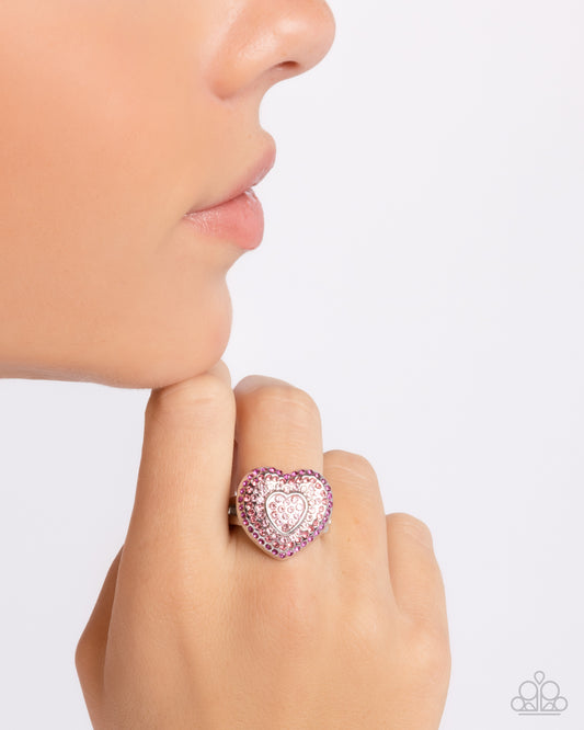 Pink heart-shaped ring on a model's finger against a white background