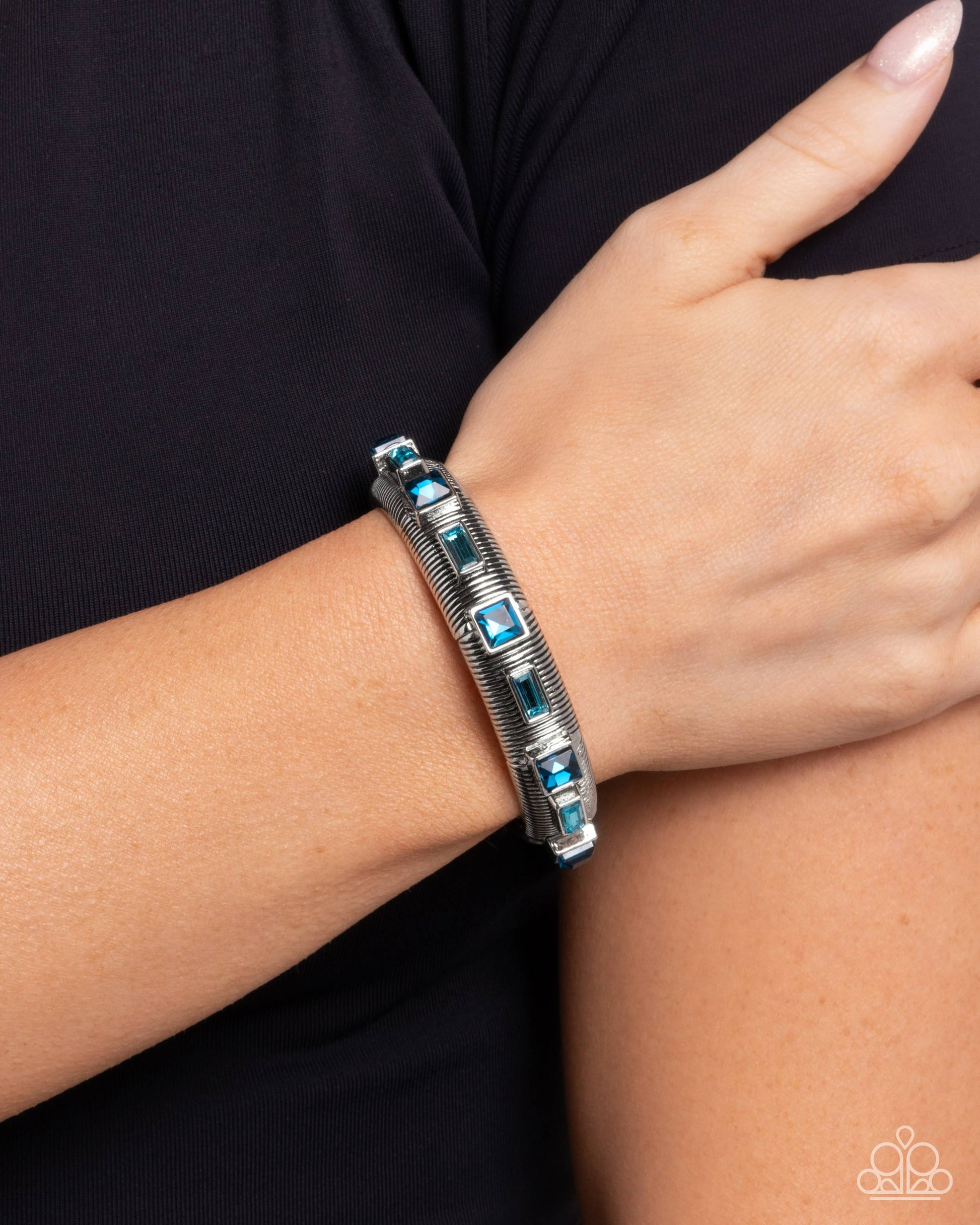 Silver bracelet with blue stones on a wrist against a black background