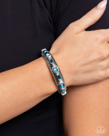 Silver bracelet with blue stones on a wrist against a black background