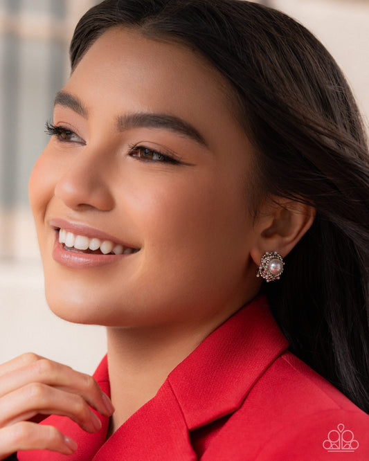 Woman wearing a red blazer with pearl earrings against a neutral background