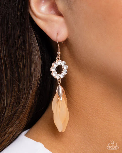 Earring with a circular design and feather-like element worn by a person.