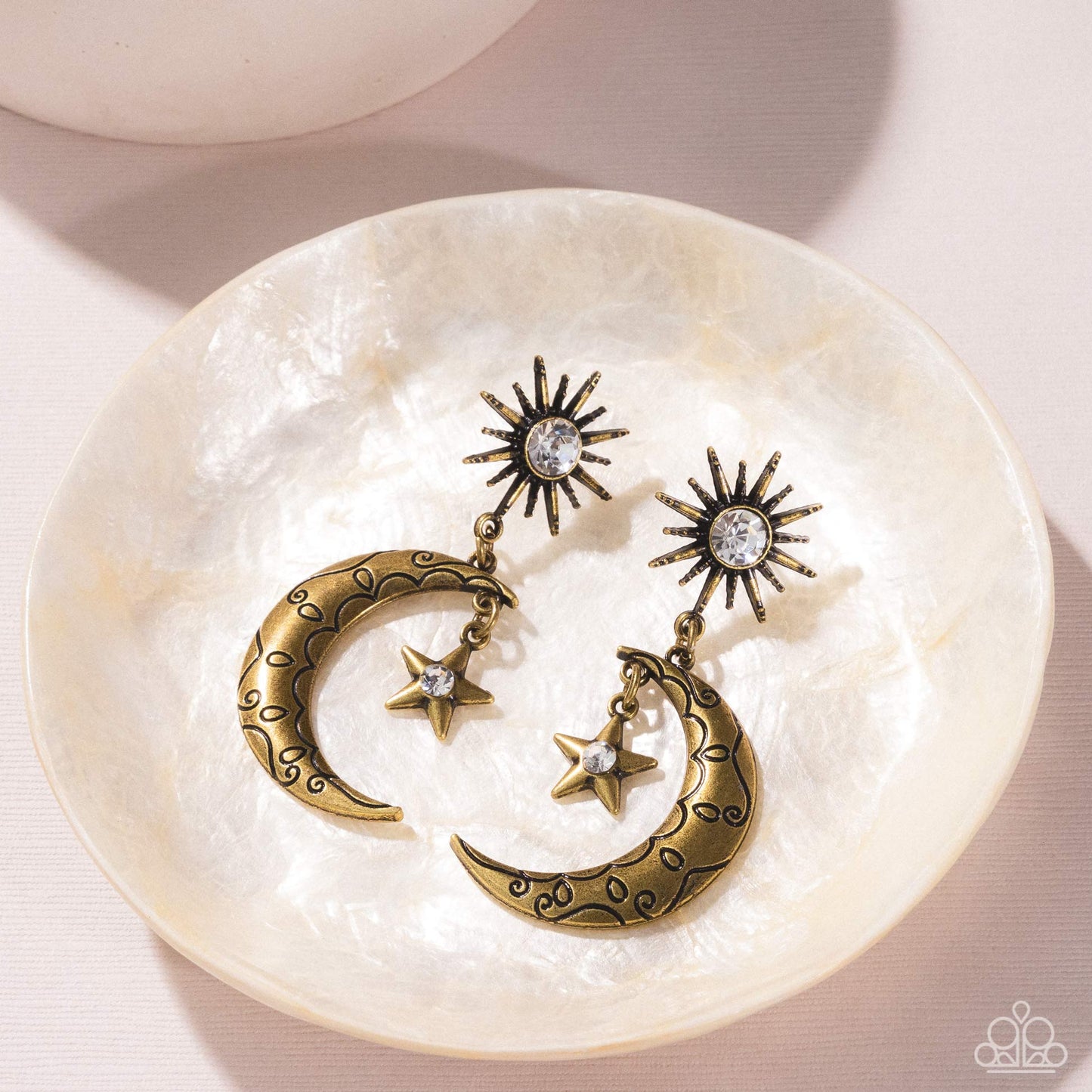 Pair of gold moon and star earrings on a white shell dish.