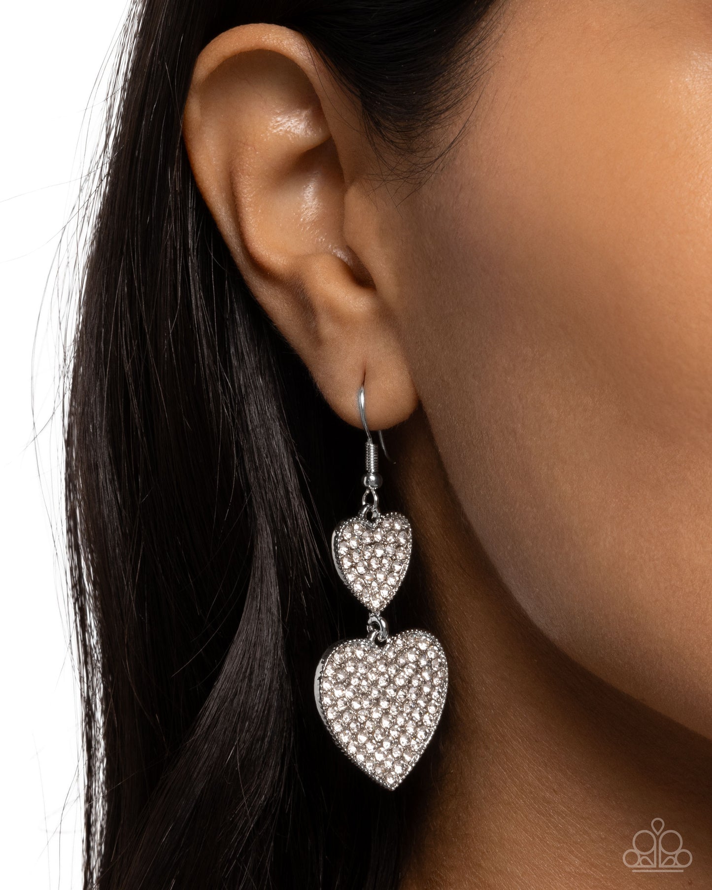 Heart-shaped earrings being worn on an ear with a neutral background