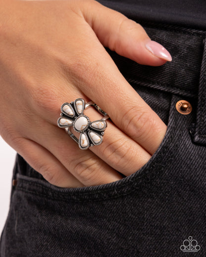 Silver floral ring on a finger with a black denim background