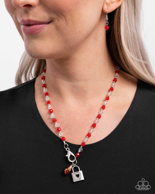Woman wearing a red and silver beaded necklace with a lock charm on a plain background