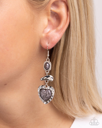 Earring with heart-shaped purple stones and silver accents worn by a person with blonde hair.