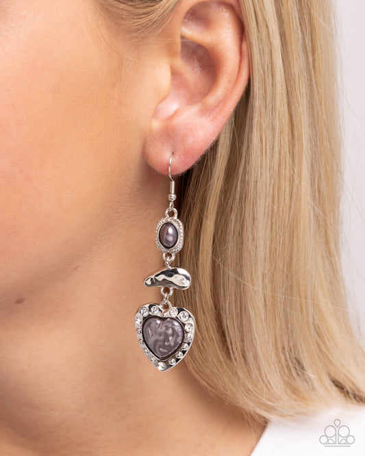 Earring with heart-shaped purple stones and silver accents worn by a person with blonde hair.