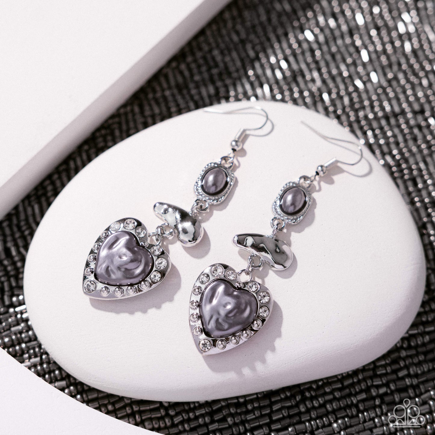 Heart-shaped earrings with gray stones on a white stone surface