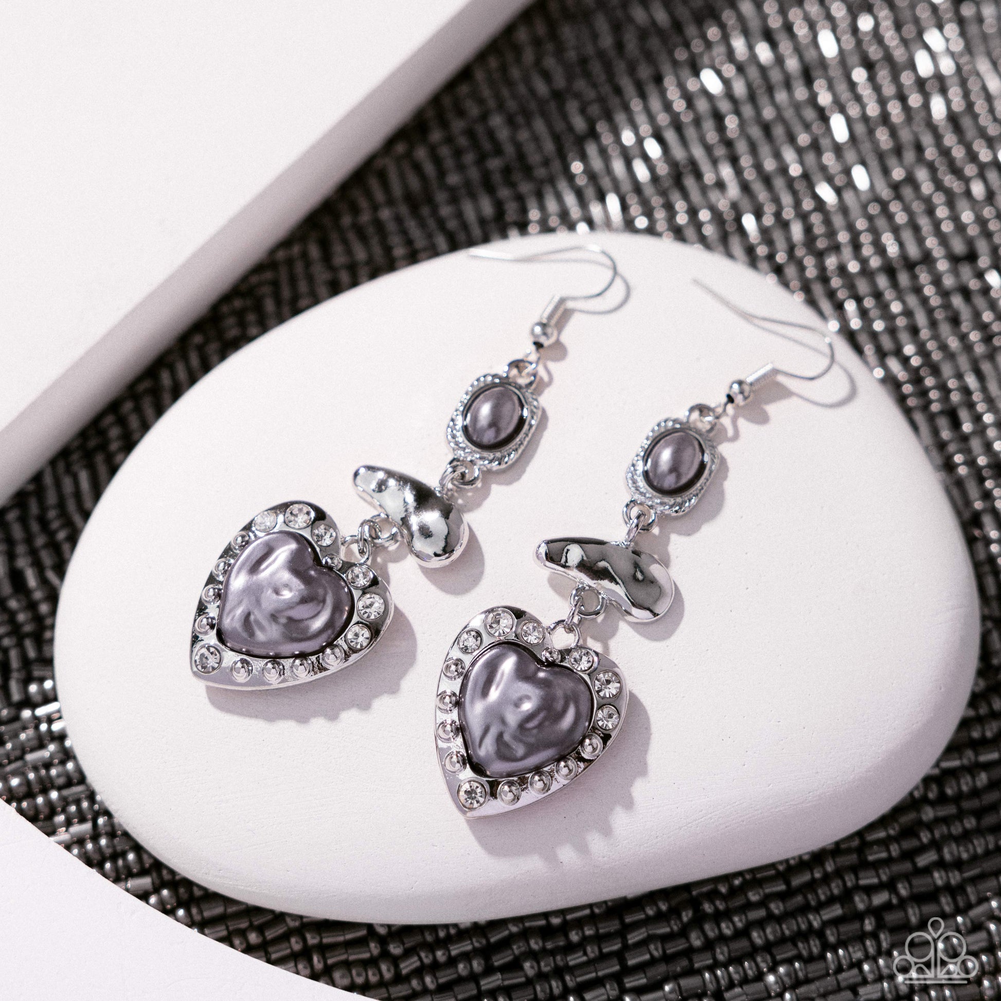 Heart-shaped earrings with gray stones on a white stone surface