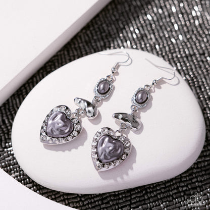 Heart-shaped earrings with gray stones on a white stone surface