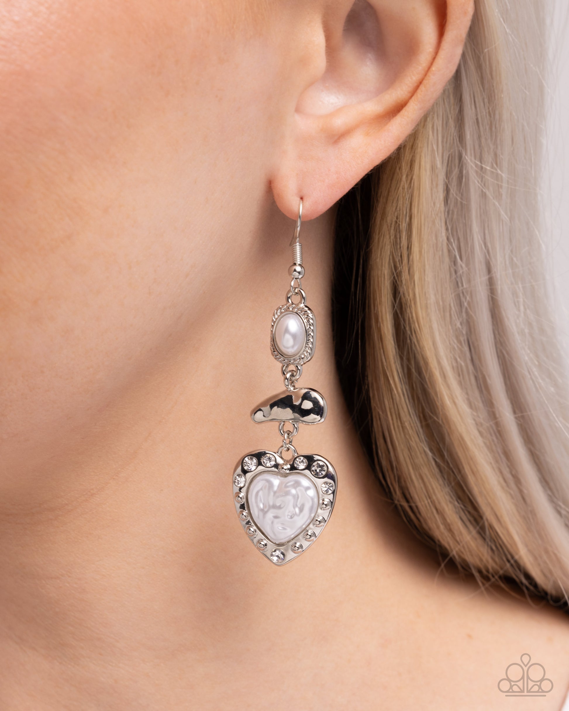 Silver heart-shaped earring with pearl-like center worn by a person