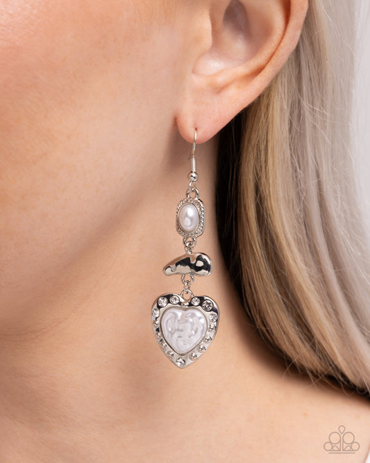 Silver heart-shaped earring with pearl-like center worn by a person