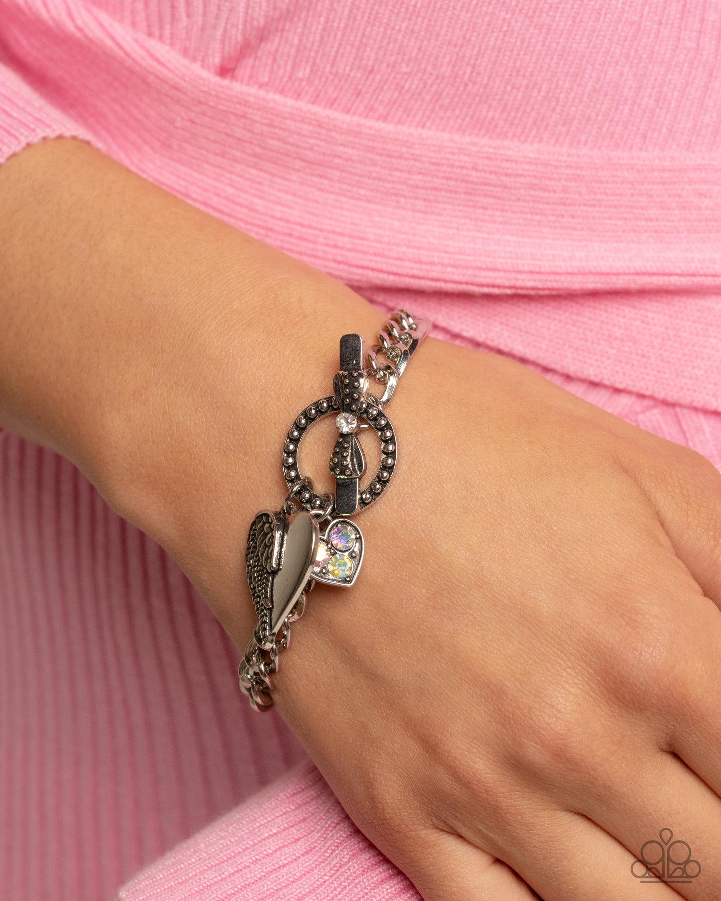 Bracelet with charms on a wrist against a pink background